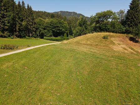 Weitläufige Grünfläche mit einem Weg, umgeben von Bäumen und sanften Hügeln im Hintergrund.