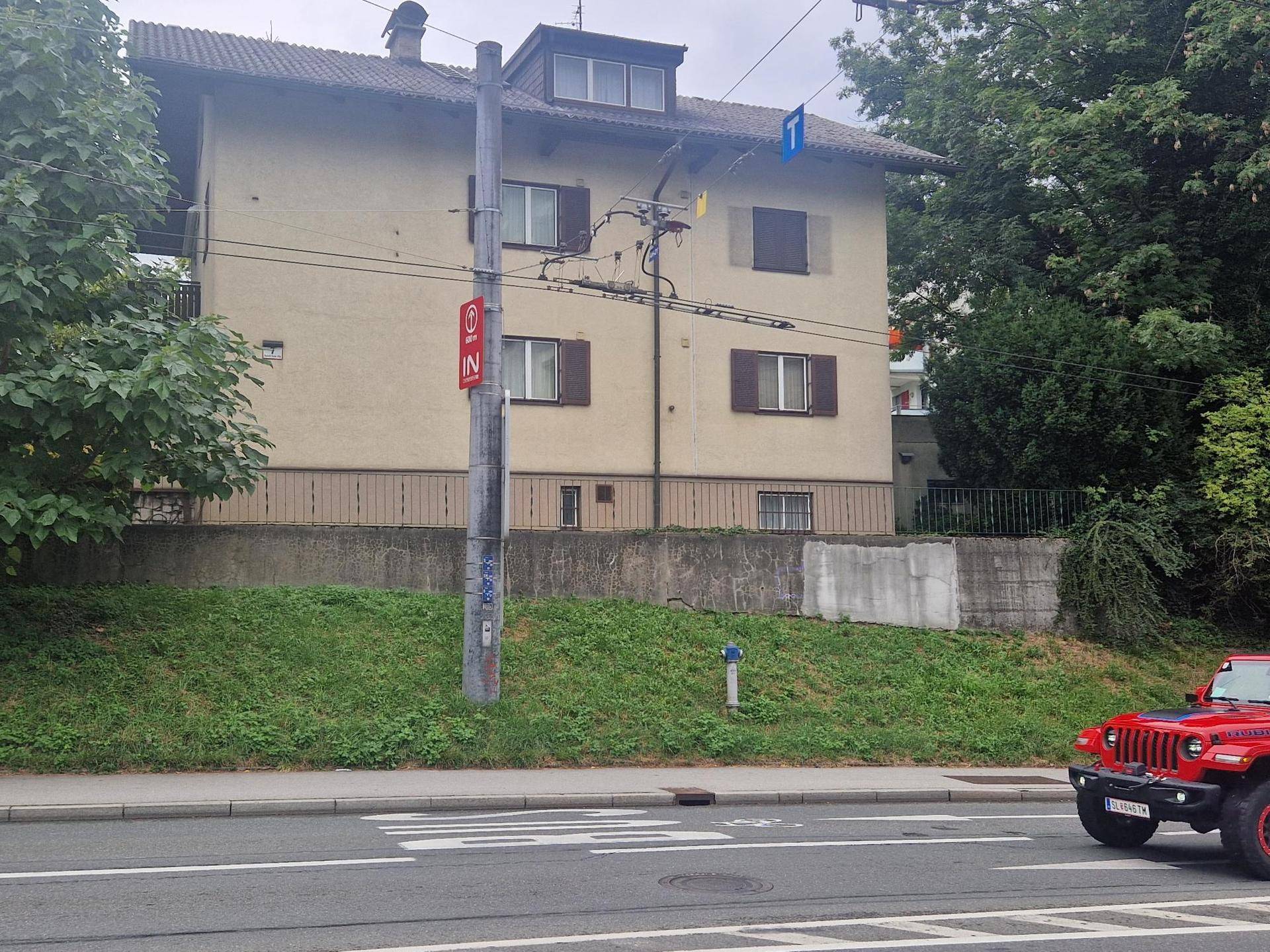 Gebäudefassade von der Straße aus gesehen mit Fenstern, Fensterläden und umgebenden Bäumen.