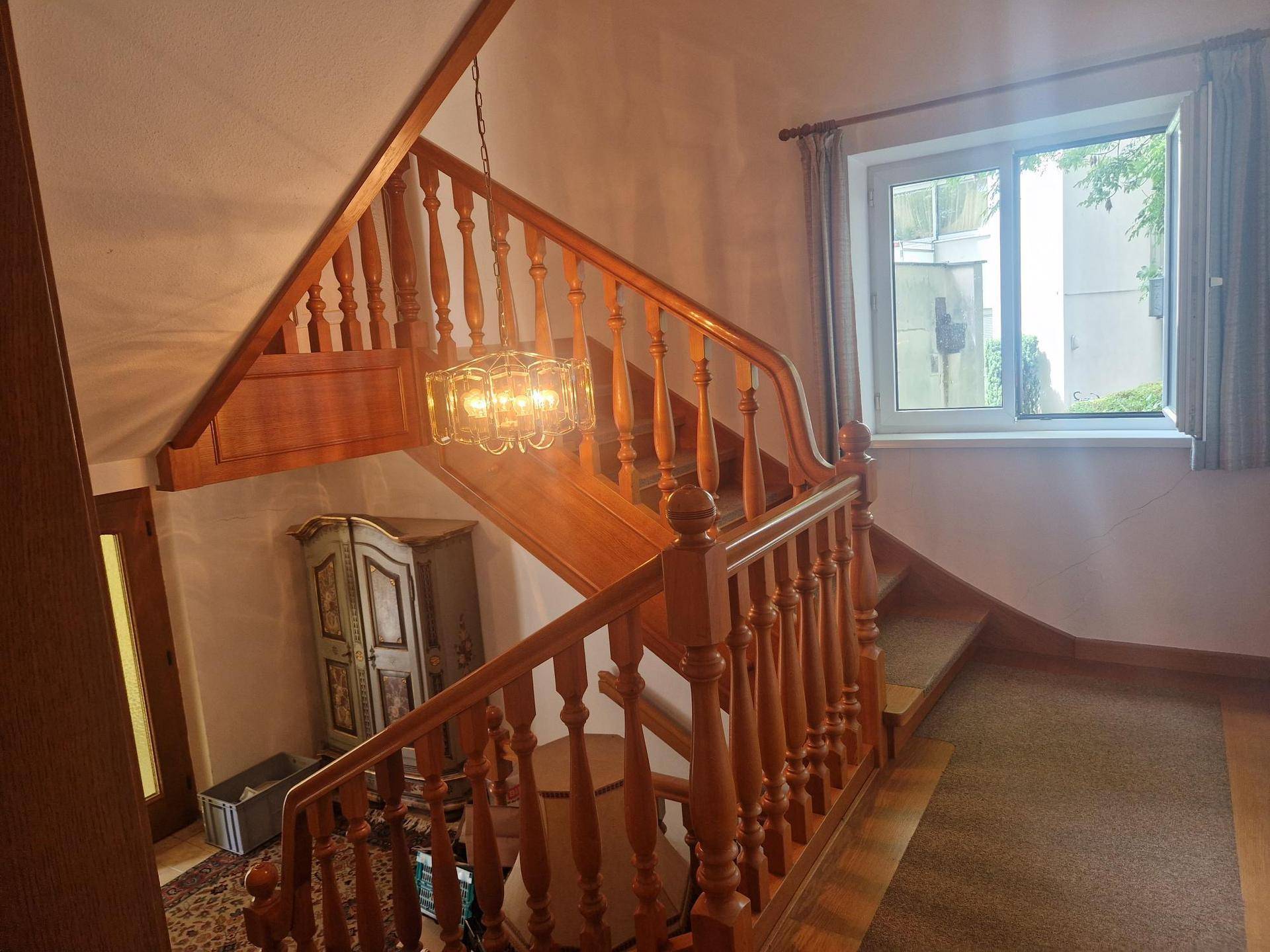 Hölzerne Treppe mit gedrechseltem Geländer, Kronleuchter und Fenster für natürliches Licht.