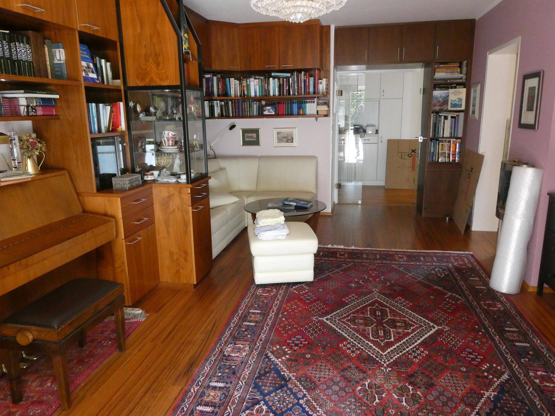 Gemütliches Wohnzimmer mit vielen Büchern, Holzmöbeln und einem beigen Sofa.