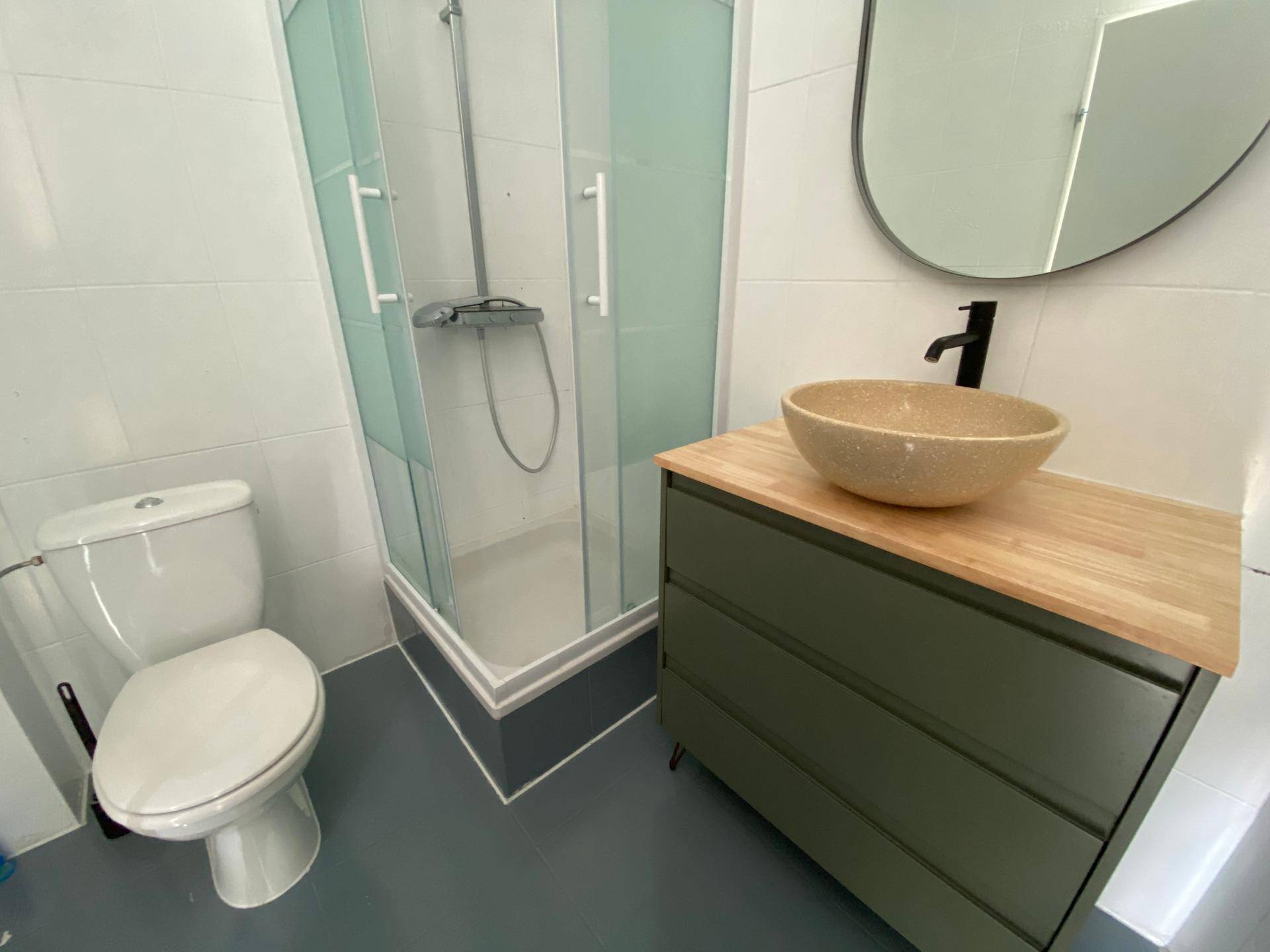 Modernes Badezimmer mit Duschkabine, WC und einem Waschbecken auf Holzplatte.