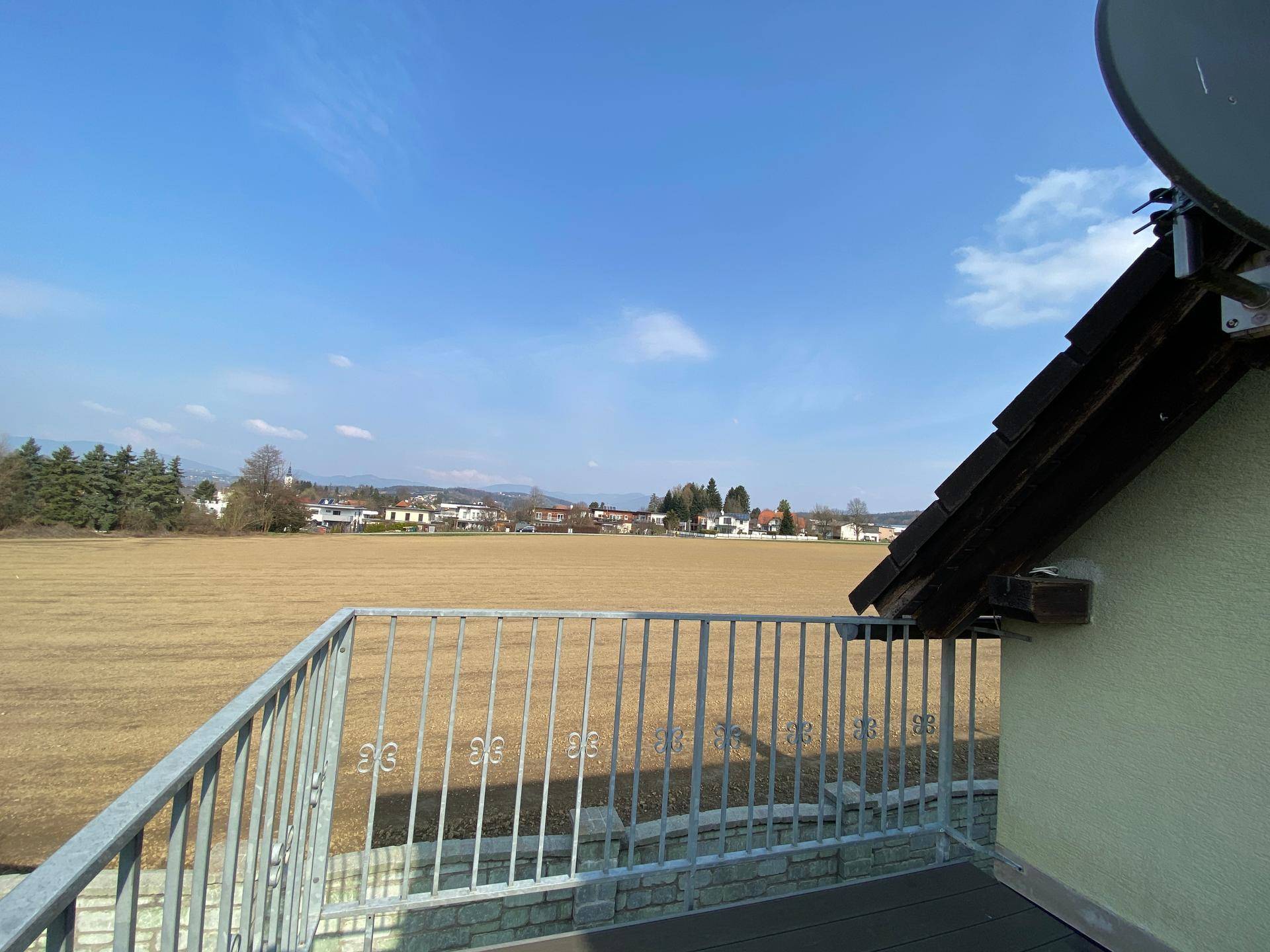 Balkon mit weitem Blick über Felder und die umliegende Landschaft unter blauem Himmel.