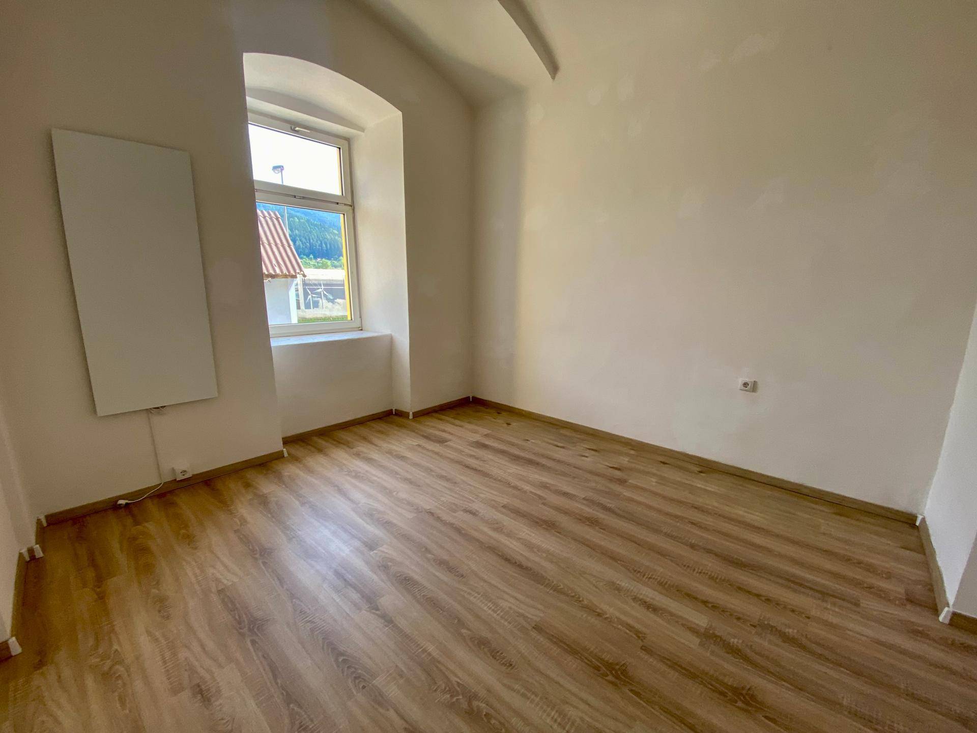 Helles Schlafzimmer mit Laminatboden, weißen Wänden und Blick auf die ländliche Umgebung.