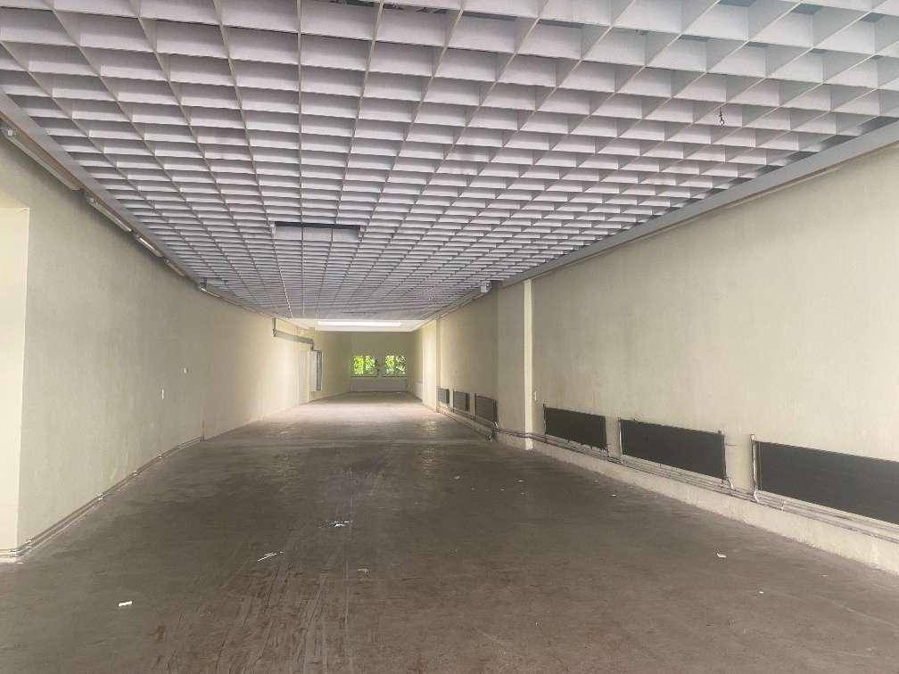 Langer, leerer Geschäftsraum mit Gitterdecke und Fenstern am Ende, bereit für die Gestaltung.