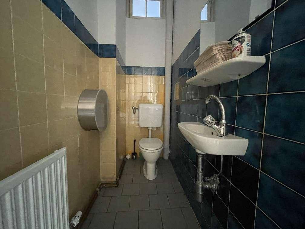 Kleiner Toilettenraum mit gelben und blauen Fliesen, einem Waschbecken und einem kleinen Fenster.