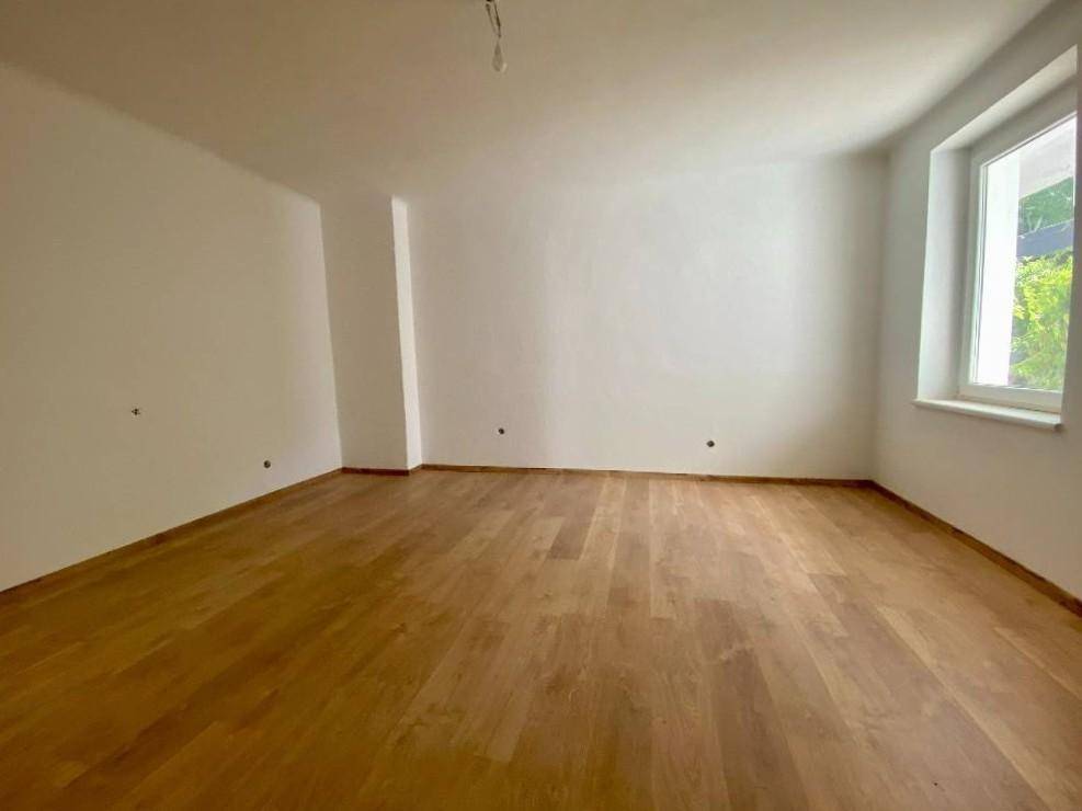 Geräumiges, leeres Zimmer mit Holzparkettboden, weißen Wänden und einem hellen Fenster.