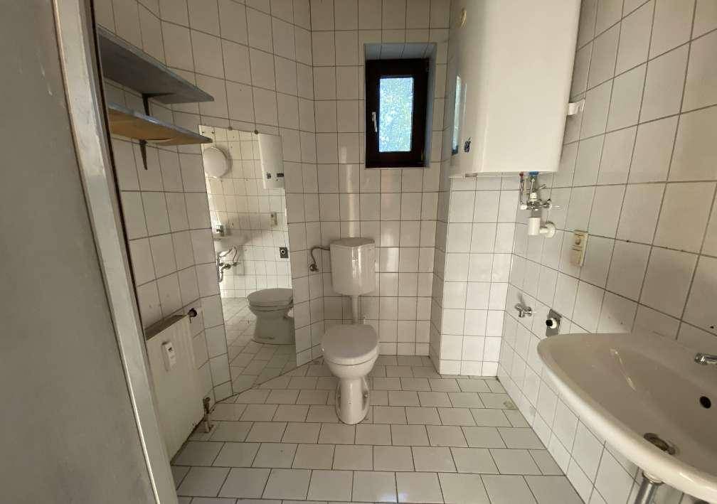 Gefliestes Badezimmer mit WC, Waschbecken, Warmwasserboiler und kleinem Fenster.