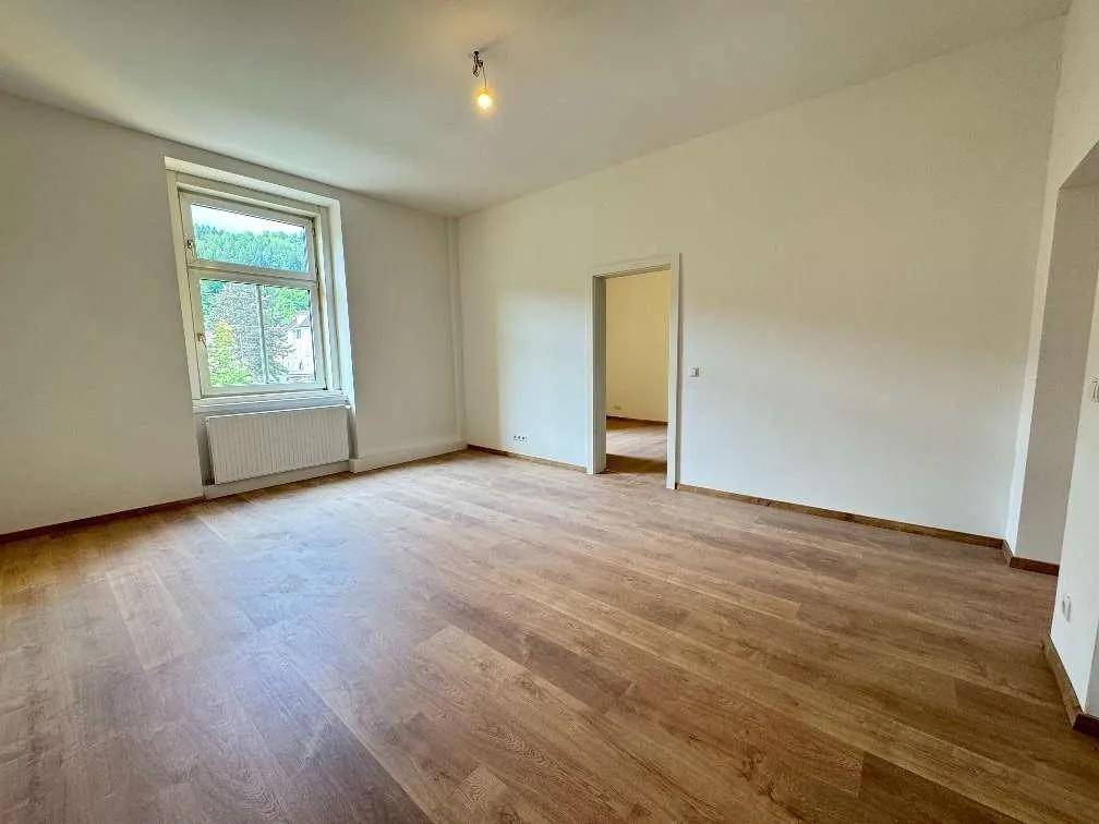 Heller, leerer Raum mit Holzparkettboden, weißen Wänden und einem großen Fenster.