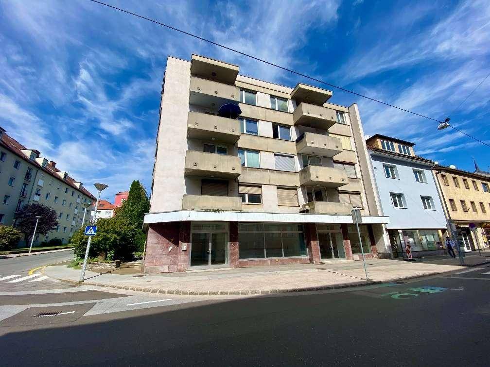 Mehrstöckiges Gebäude an einer Straßenecke mit mehreren Balkonen und einer Fassade, die eine Renovierung benötigt.