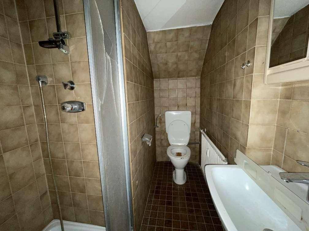 Funktionales Badezimmer mit braunen Wand- und Bodenfliesen, einer Dusche, Toilette und einem Waschbecken.