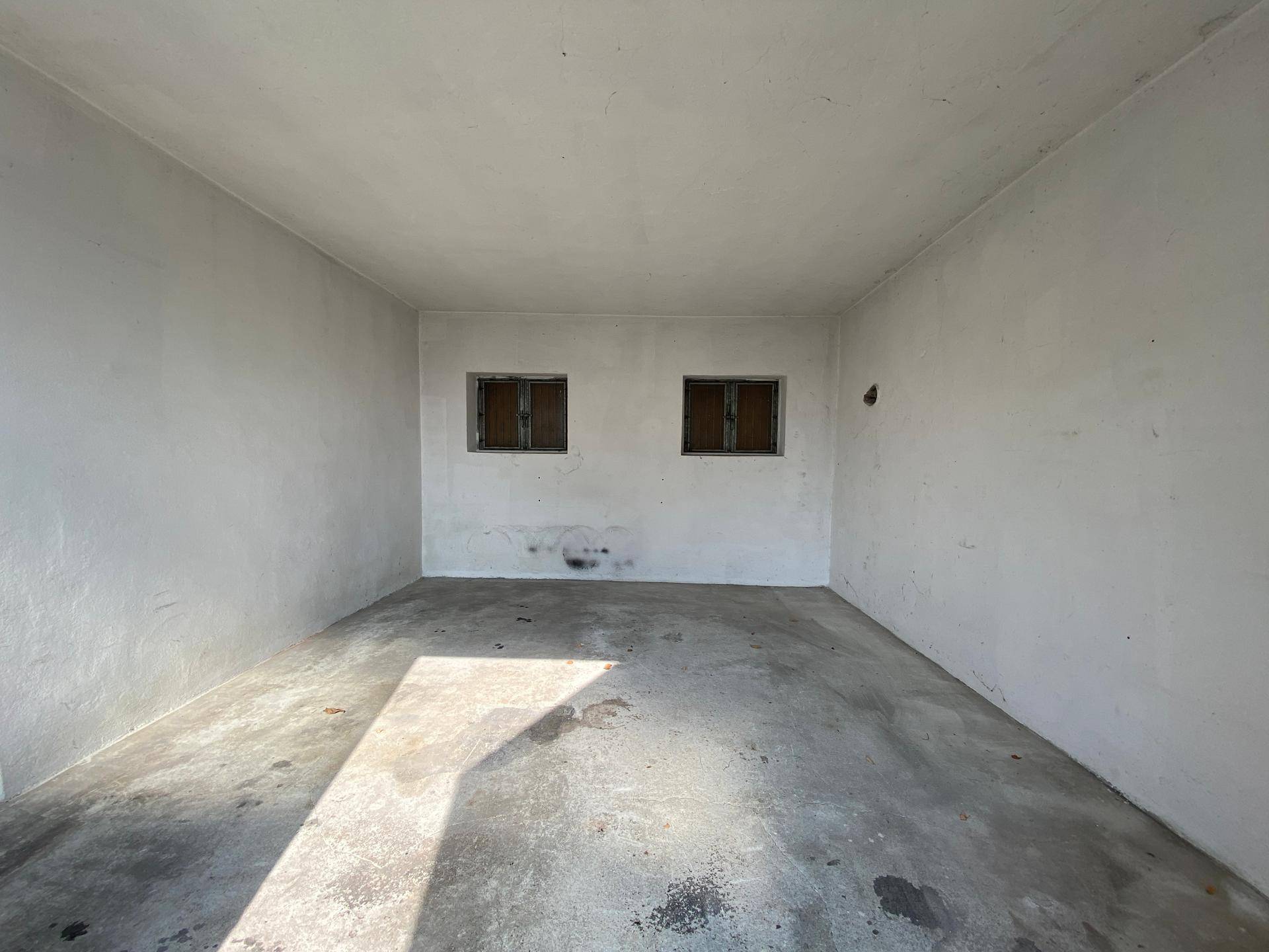 Leere Garage mit Betonboden und zwei kleinen Fenstern.