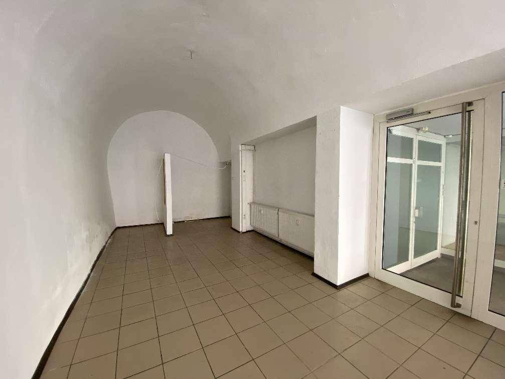 Leerer Gewerberaum mit gefliestem Boden, gewölbter Decke und großen Glastüren, bereit zur Renovierung.