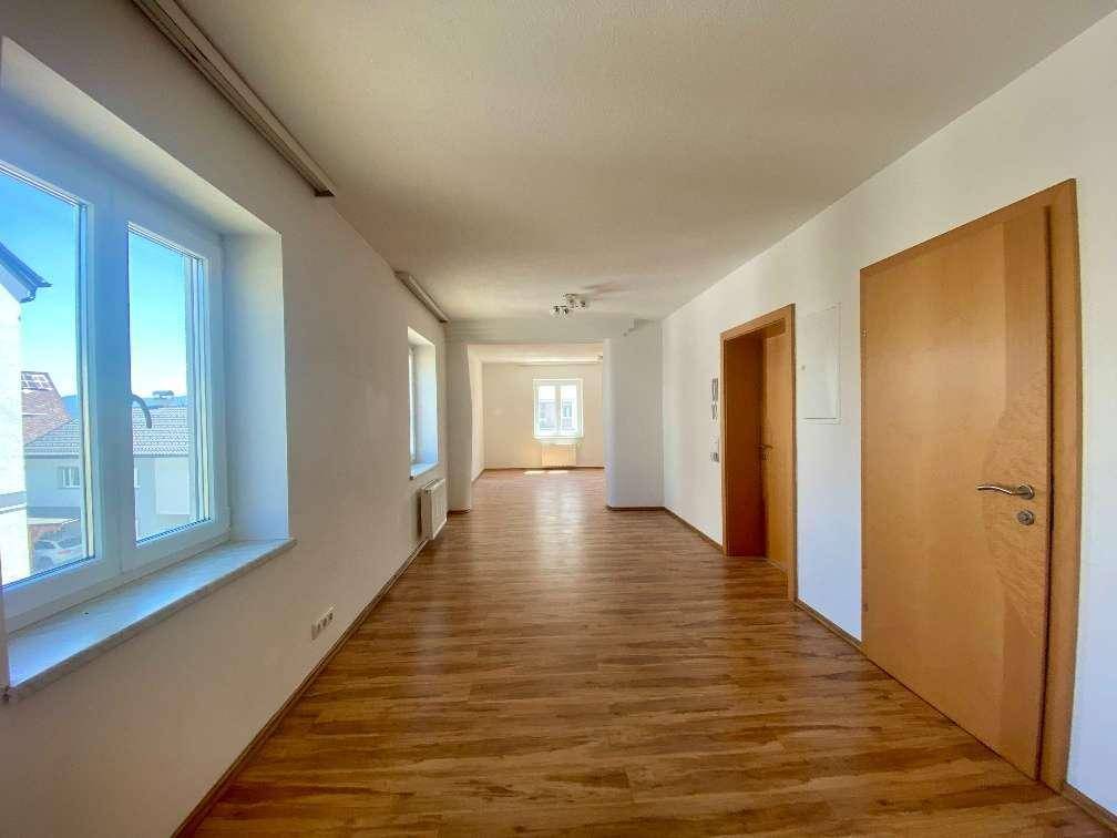 Heller Flur mit Holzfußboden und mehreren Fenstern, der zu weiteren Räumen führt.