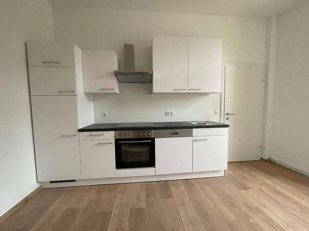 Moderne Einbauküche mit weißen Schränken, dunkler Arbeitsplatte und integrierten Geräten.