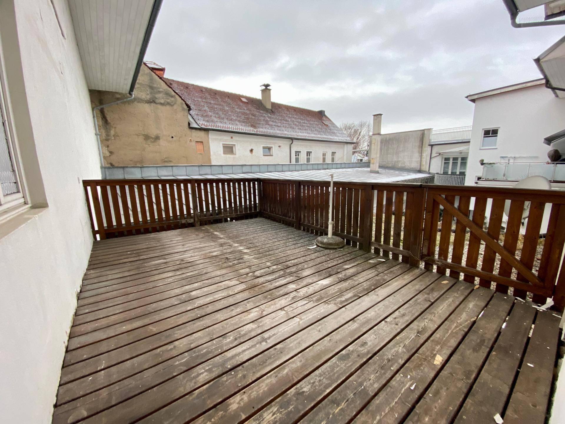 Große Holzterrasse mit Holzzaun und Blick auf die umliegenden Dächer und Gebäude.