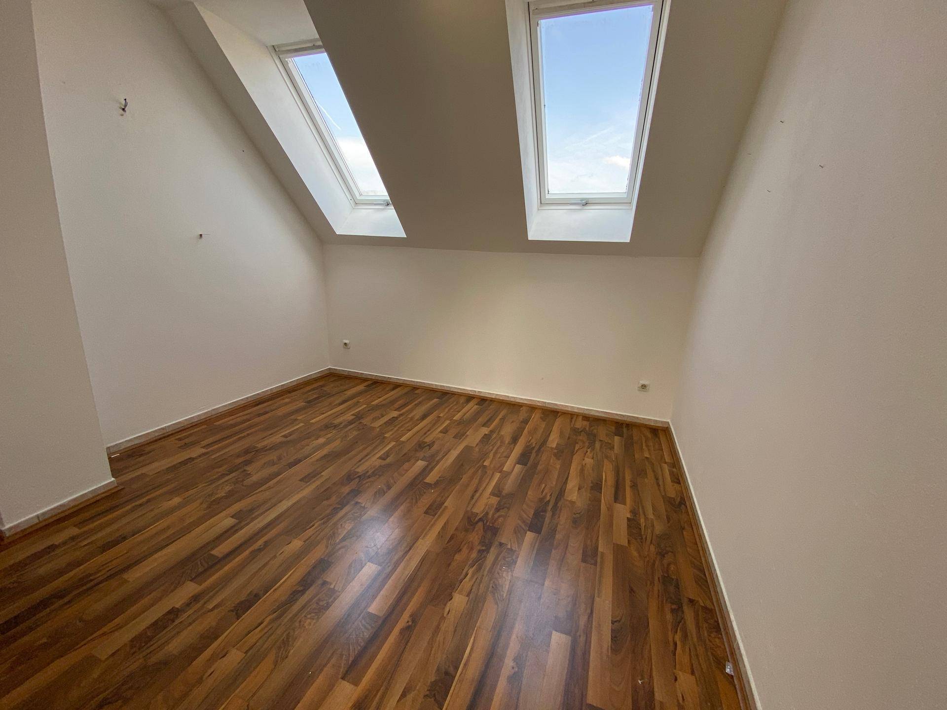 Schlafzimmer im Dachgeschoss mit Laminatboden und zwei hellen Dachfenstern.