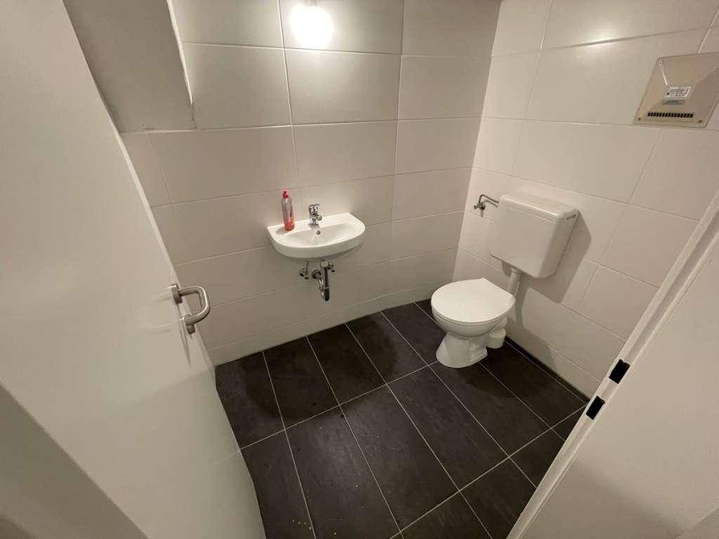 Kompakte Toilette mit weißem Waschbecken, dunklem Fliesenboden und Abluftventilator.