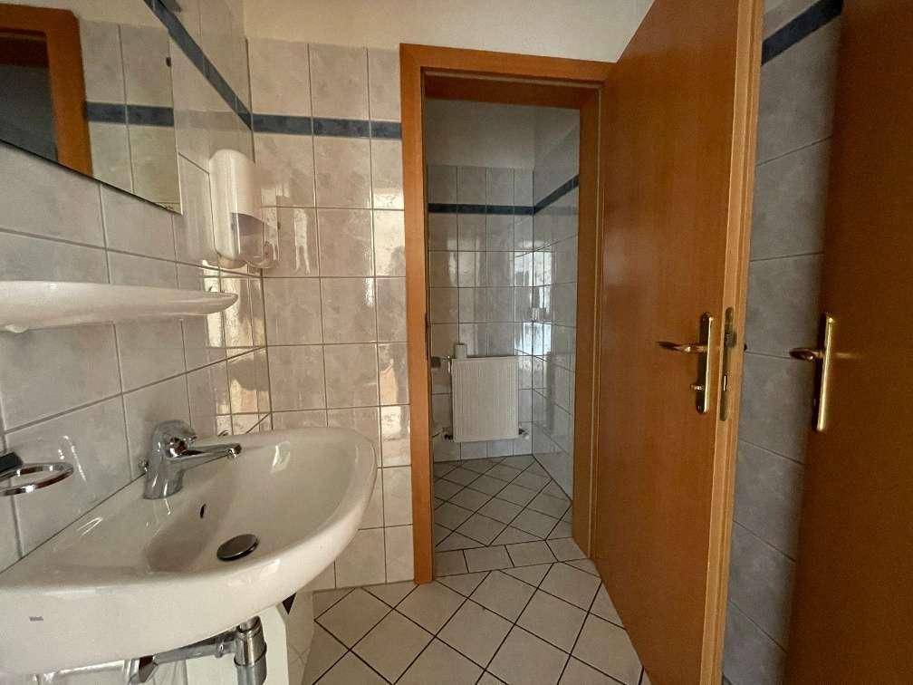 Badezimmer mit Waschbecken und gefliesten Wänden, angrenzend an einen weiteren Raum.