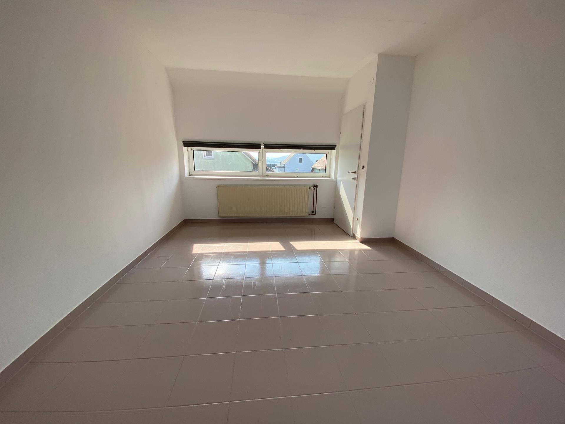Helles Zimmer mit Fliesenboden und einem breiten Fenster, das Tageslicht hereinlässt.