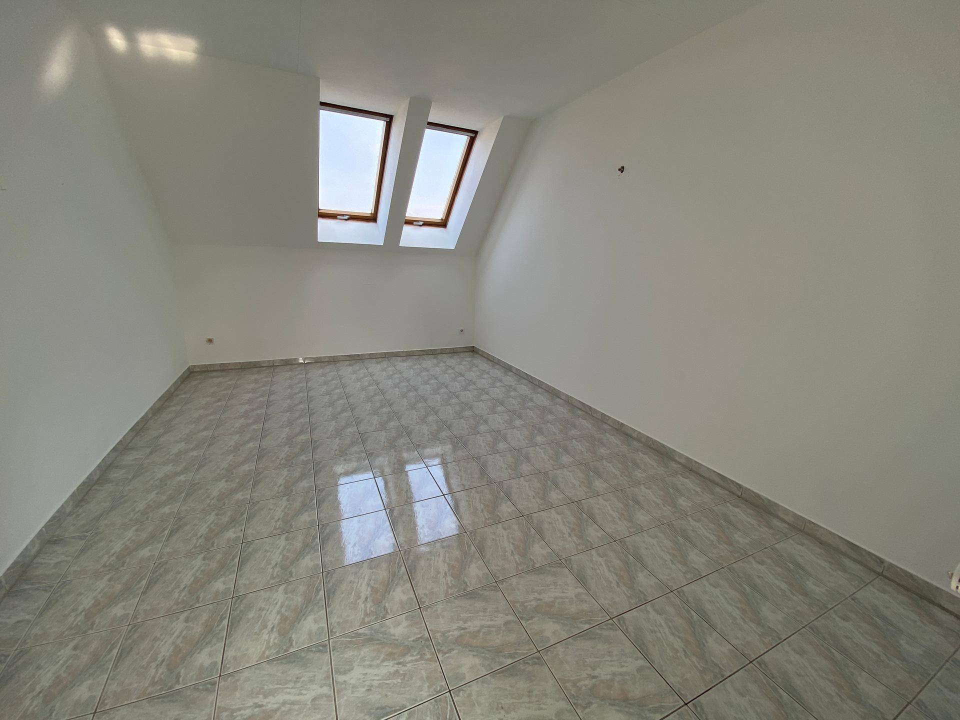 Helles Dachgeschosszimmer mit Fliesenboden und zwei großen Dachfenstern.