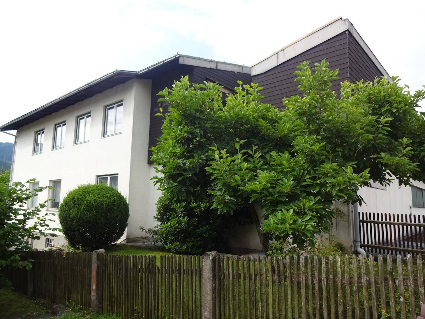 Seitenansicht des Hauses mit grüner Bepflanzung und Holzzaun.