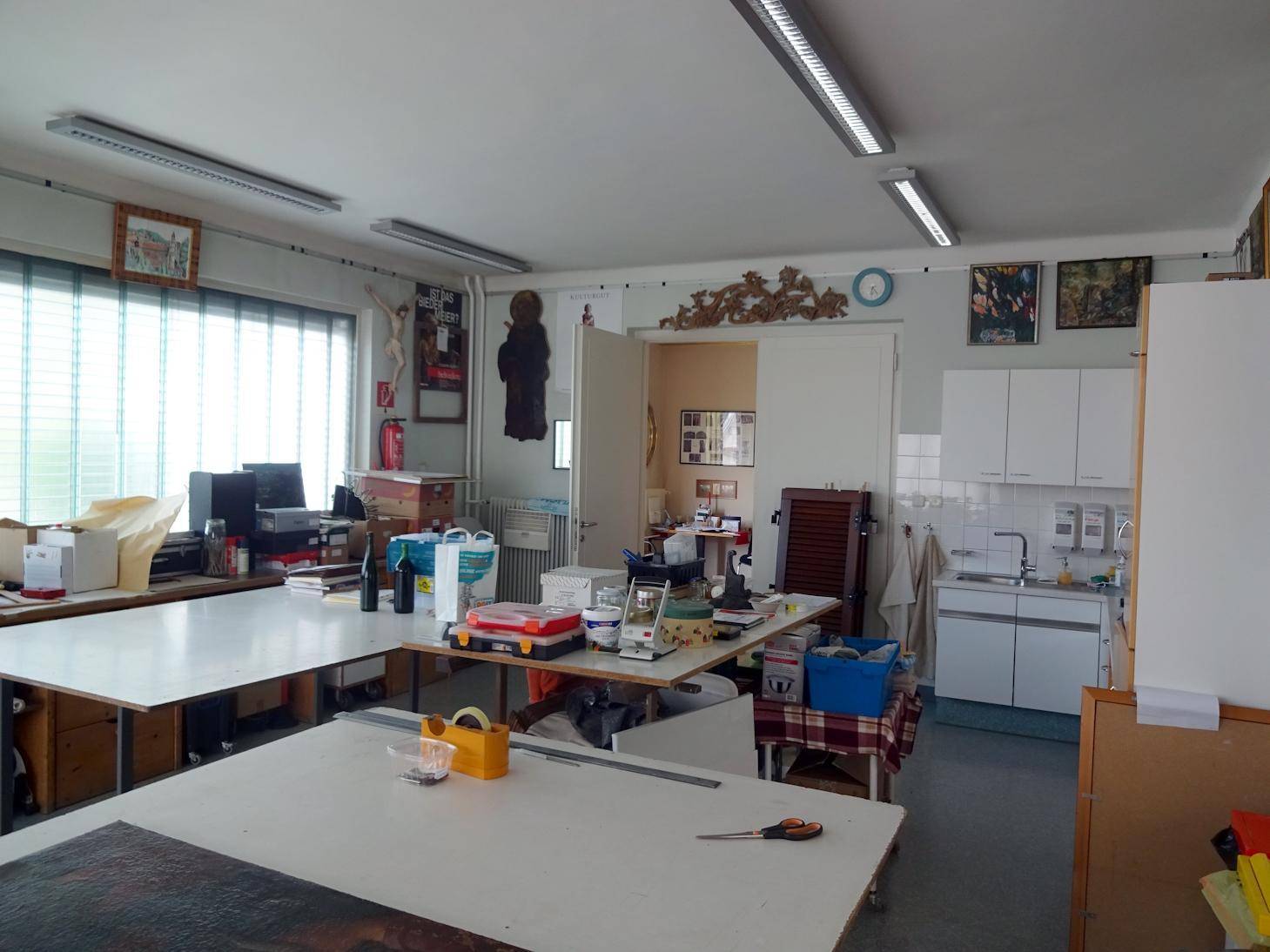 Geräumiger Arbeitsraum mit großen Tischen, viel Tageslicht und kleiner Küchenzeile.