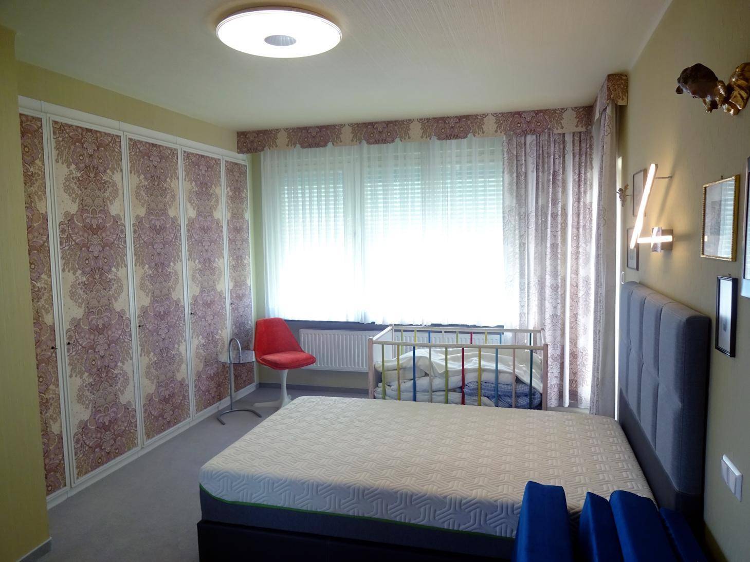 Helles Schlafzimmer mit großem Fenster, Einbauschränken und Babybett.