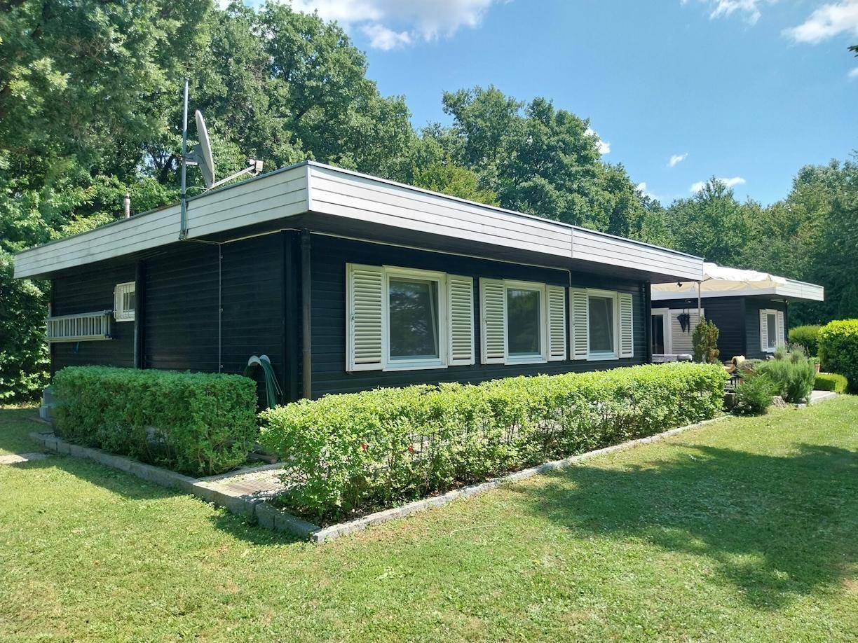 Seitenansicht des schwarzen Hauses mit weißen Fensterläden und gepflegter Hecke im grünen Garten.