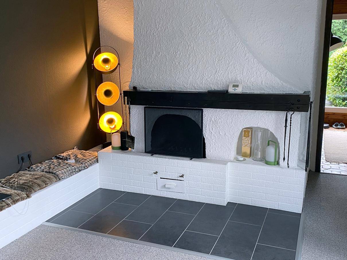 Gemütlicher Kaminbereich mit weißem Ziegelstein und dunklem Sims, umgeben von warmem Licht.