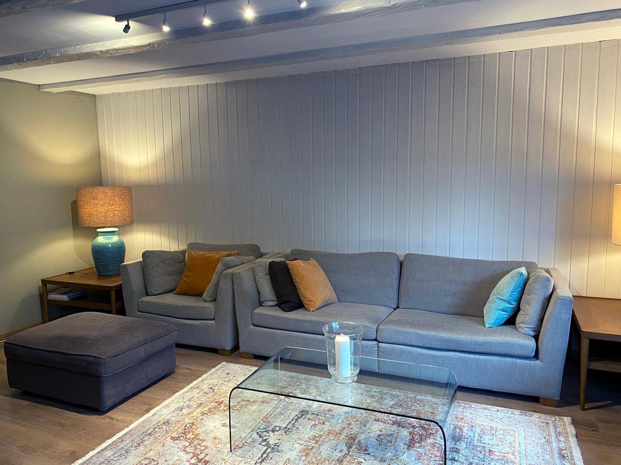 Gemütliches Wohnzimmer mit grauem Sofa, Holzbalkendecke und warmem Licht für entspannte Abende.
