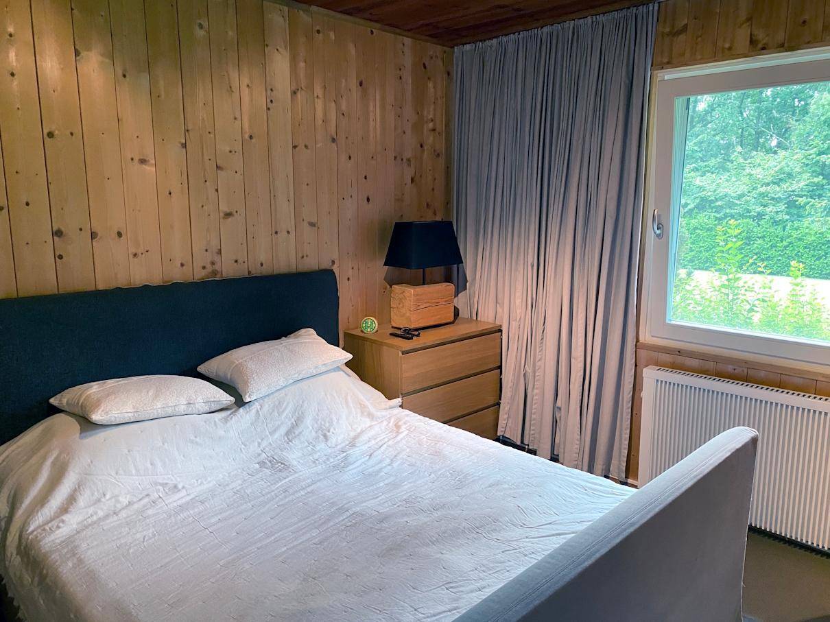 Schlafzimmer mit Holzwänden und -decke, gemütlichem Bett und Fenster mit Blick ins Grüne.