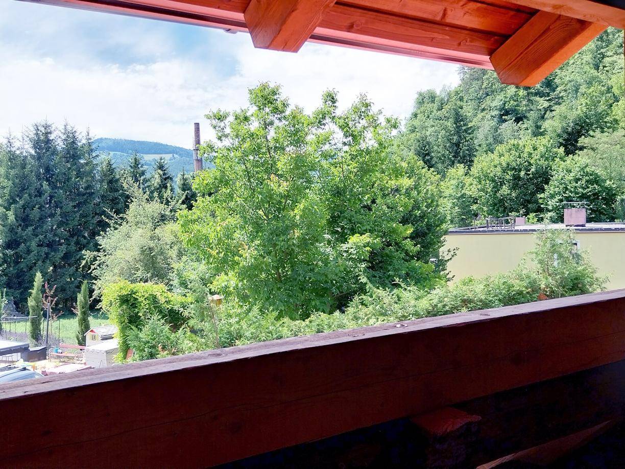 Blick aus einem Fenster mit Holzbalken auf grüne Bäume und die umliegende Natur.