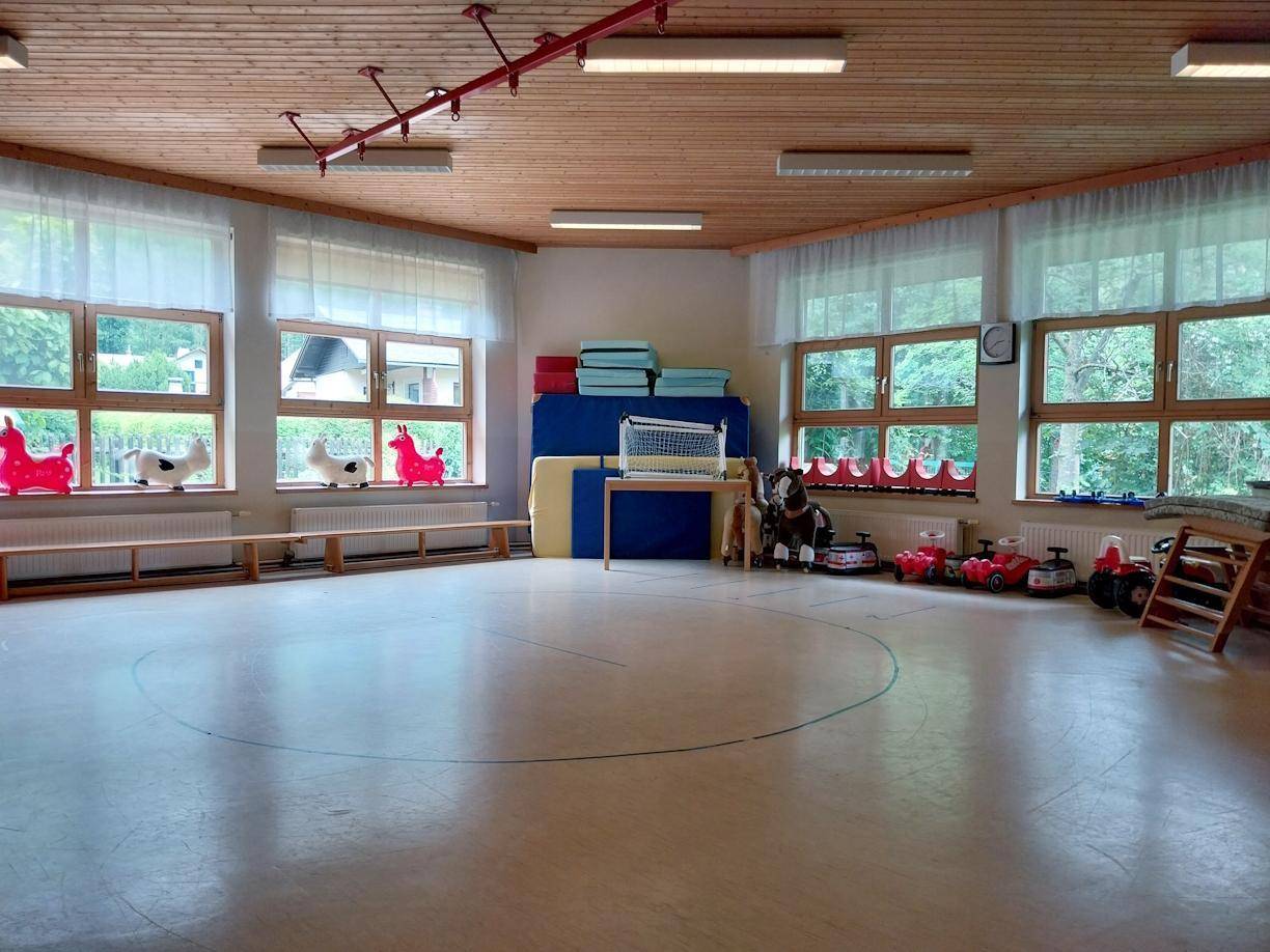 Großer Mehrzweckraum mit Holzboden, runder Markierung, vielen Fenstern und Holzdecke.