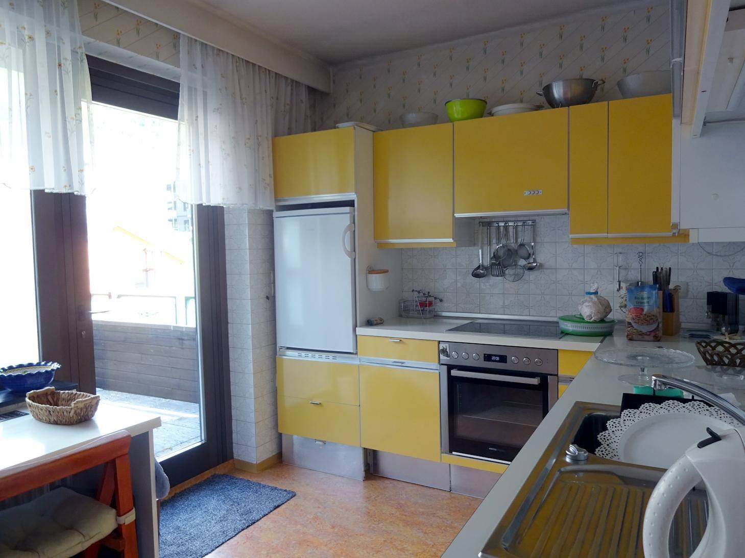 Helle Küche mit gelben Schränken, Einbaugeräten und Zugang zum Balkon.