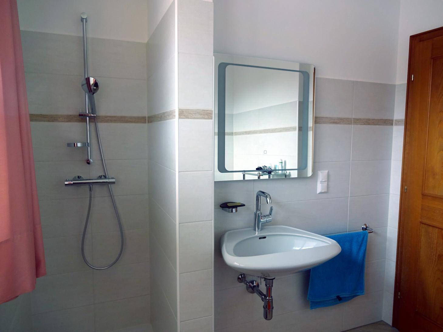 Modernes Badezimmer mit Dusche, Waschbecken und hellen Fliesen.