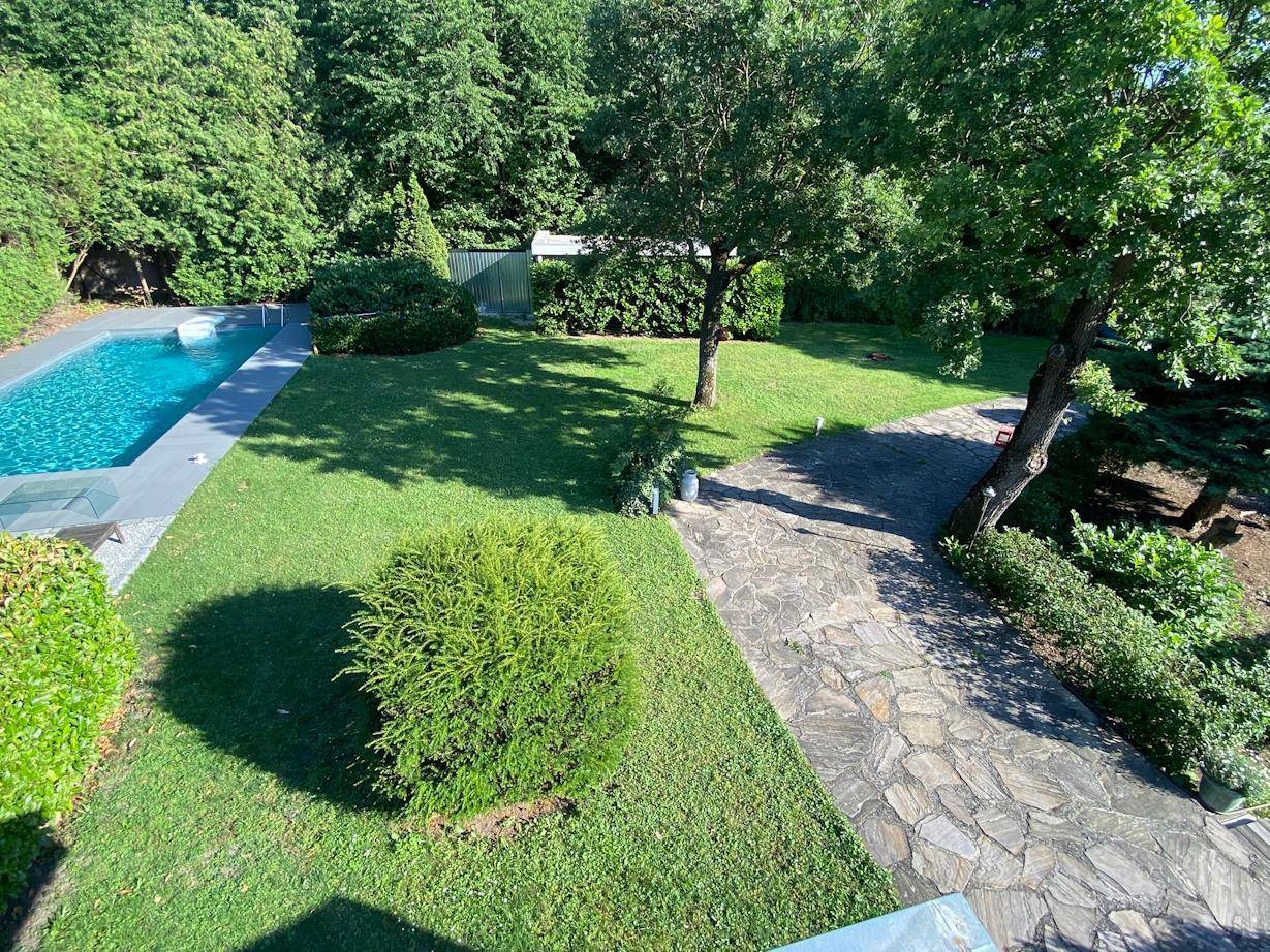Weitläufiger Gartenbereich mit Schwimmbad, gepflegtem Rasen, Steinweg und altem Baumbestand.