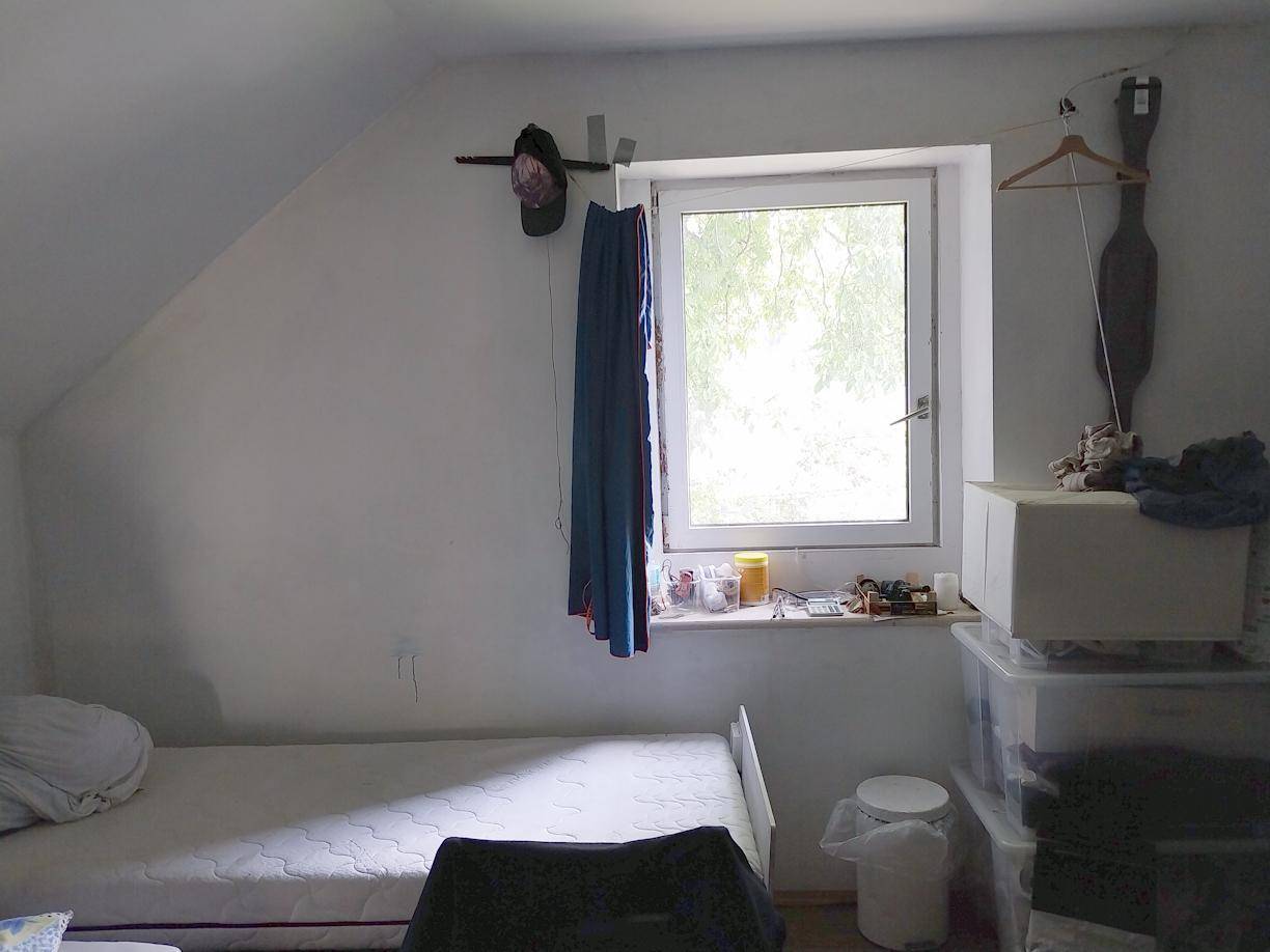 Einfaches Schlafzimmer mit Einzelbett, Dachschräge und Fenster mit Blick ins Grüne.