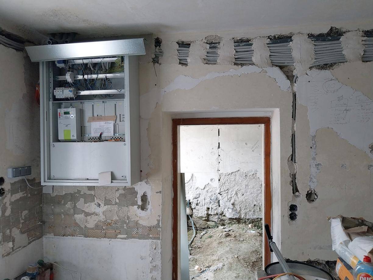 Raum in Renovierung mit freigelegten Elektroleitungen, einem Sicherungskasten und einem Türrahmen.