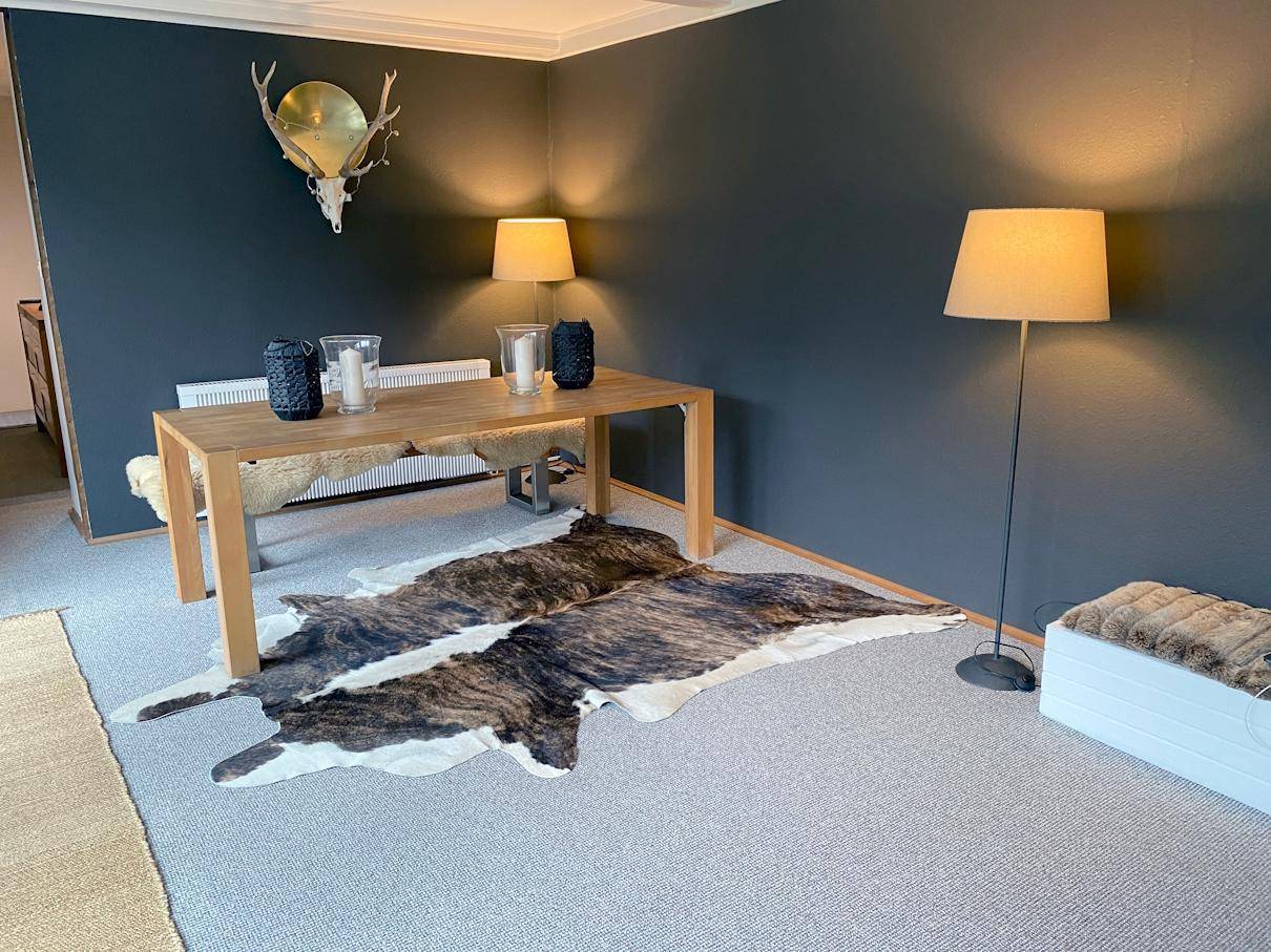 Essbereich mit Holztisch, dunklen Wänden und Teppichboden, dekoriert mit Hirschgeweih und Stehleuchte.