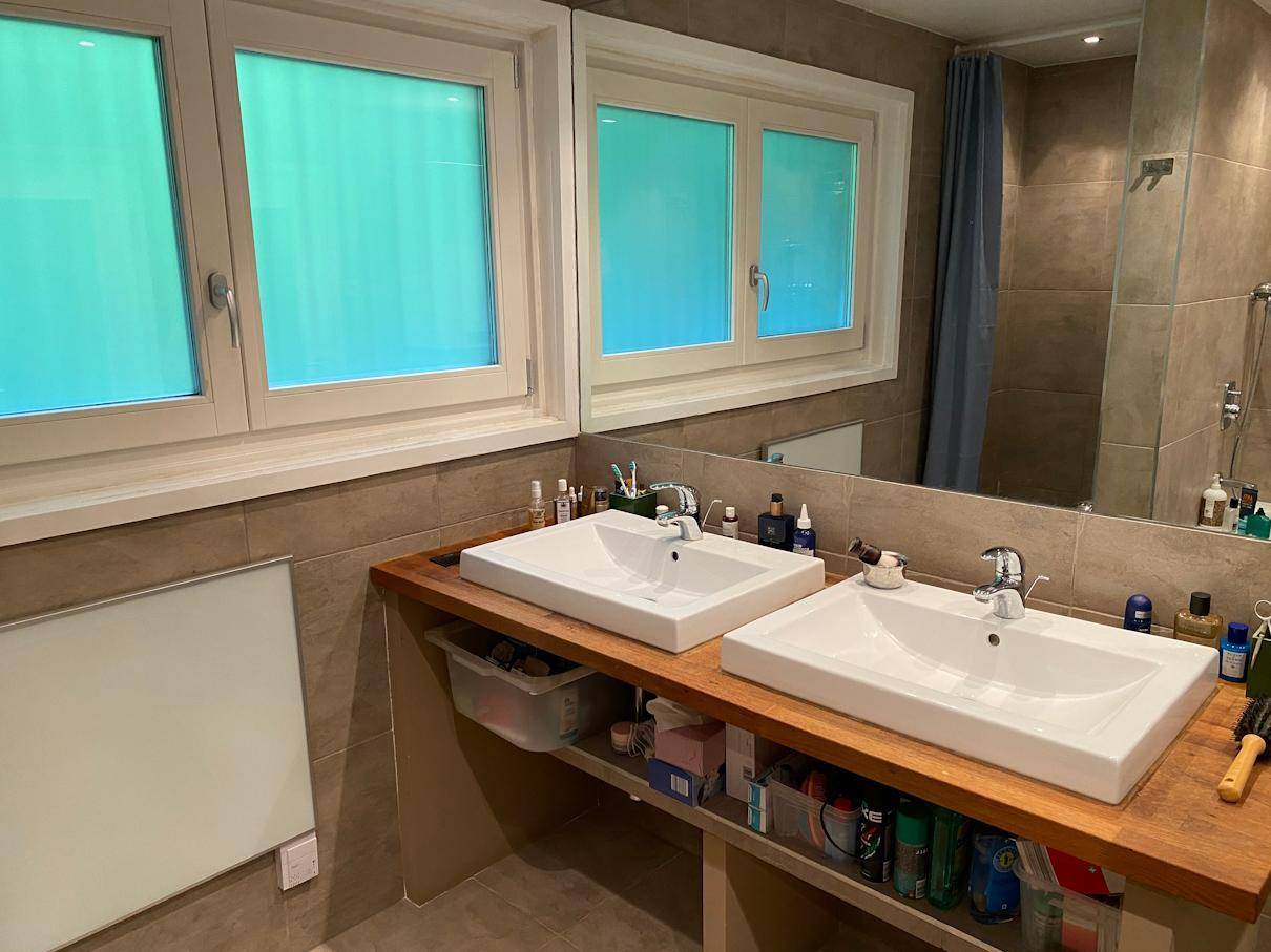 Modernes Badezimmer mit Doppelwaschbecken, großem Spiegel und Fliesenwänden, hell und funktional.