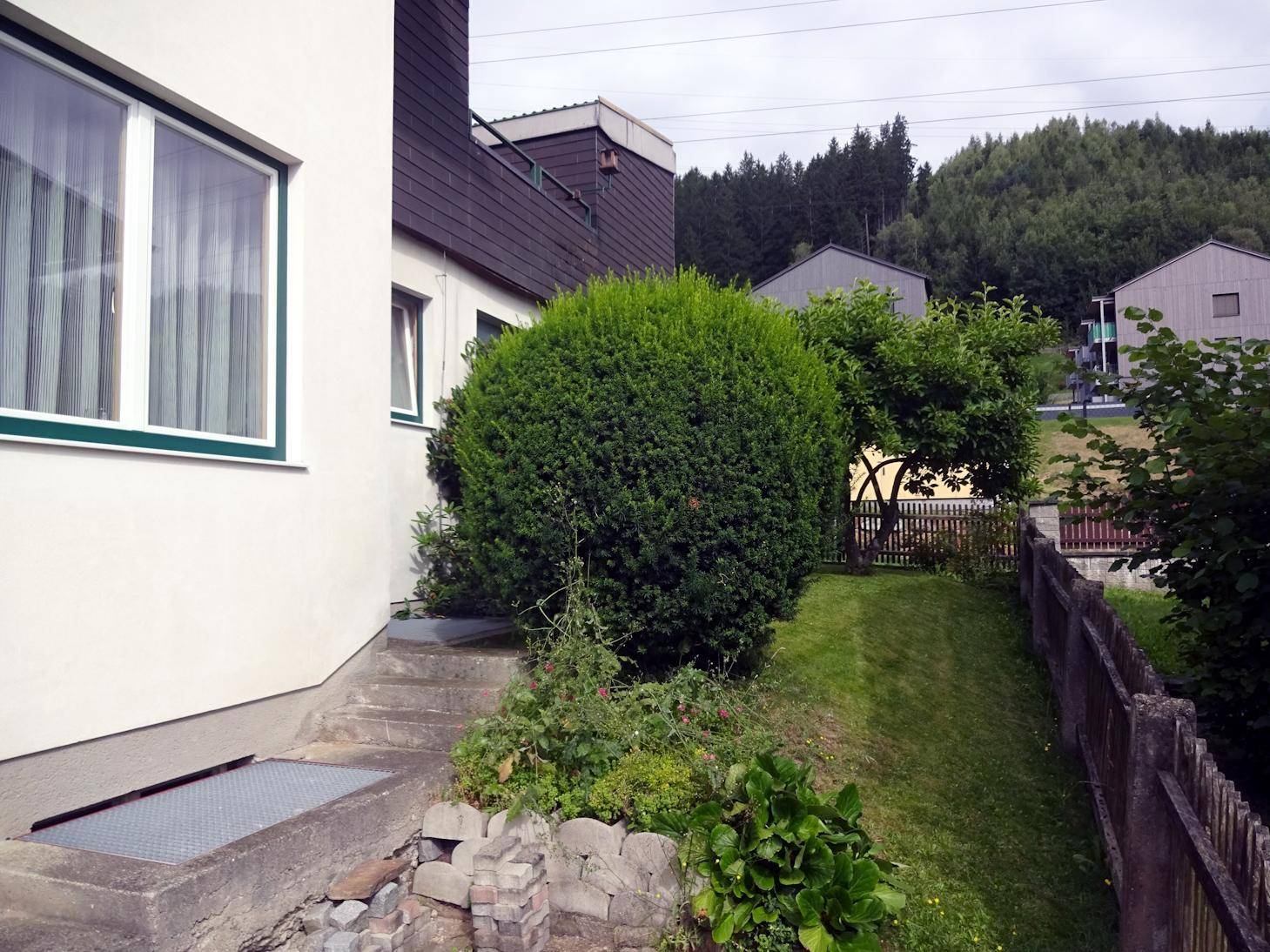 Gebäudeseite mit Treppe, gepflegter Hecke und Zugang zum Gartenbereich.