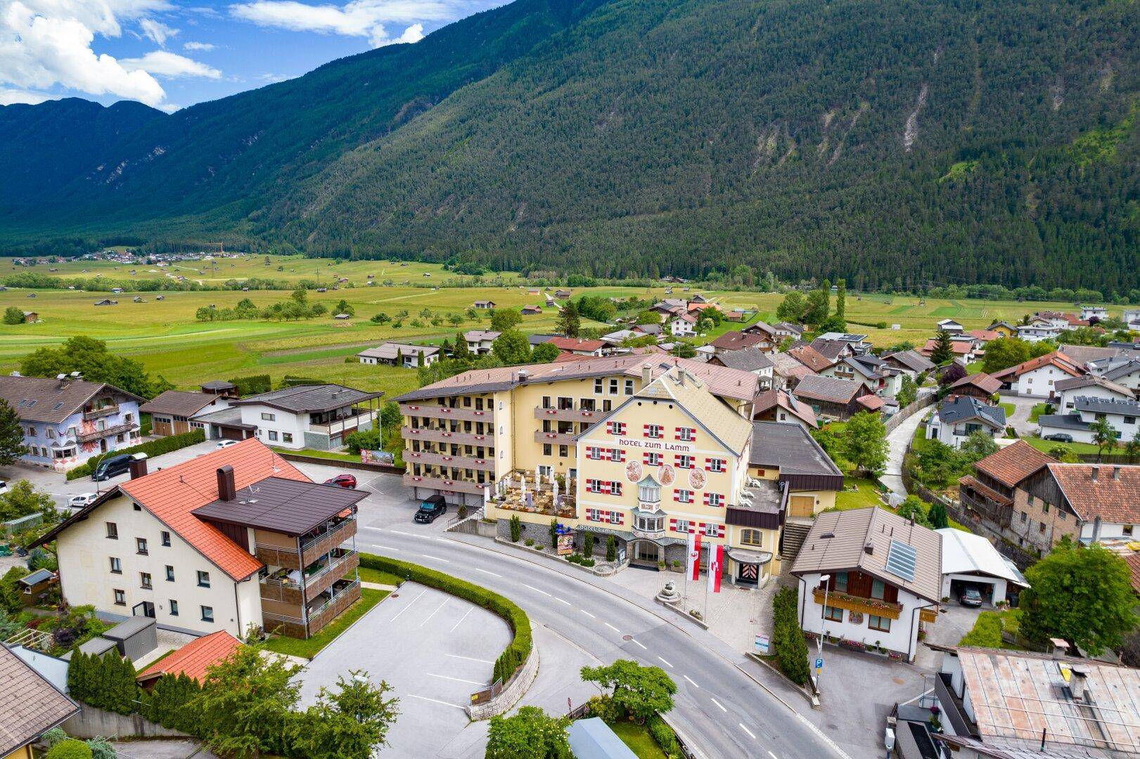 Luftaufnahme des Hotels im Zentrum eines malerischen Dorfes, eingebettet in eine weite grüne Tallandschaft.