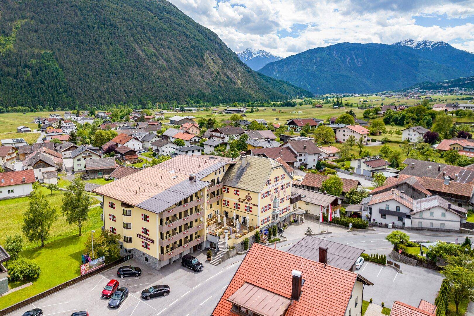 Weitläufige Luftaufnahme des Hotels und des Dorfes, umgeben von üppiger Natur und majestätischen Bergen.