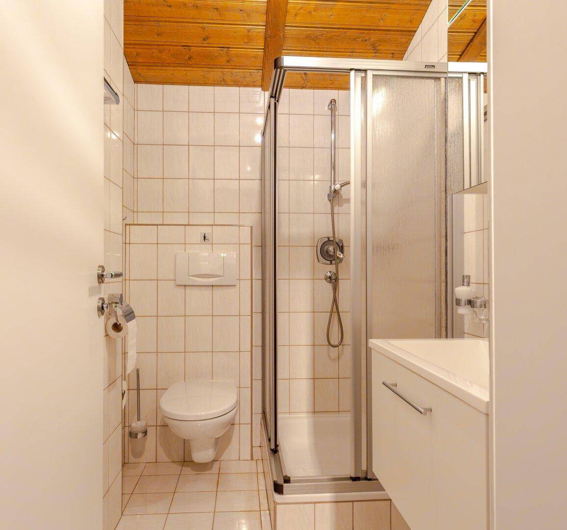 Kleines Badezimmer mit Duschkabine, WC und hellen Fliesen.