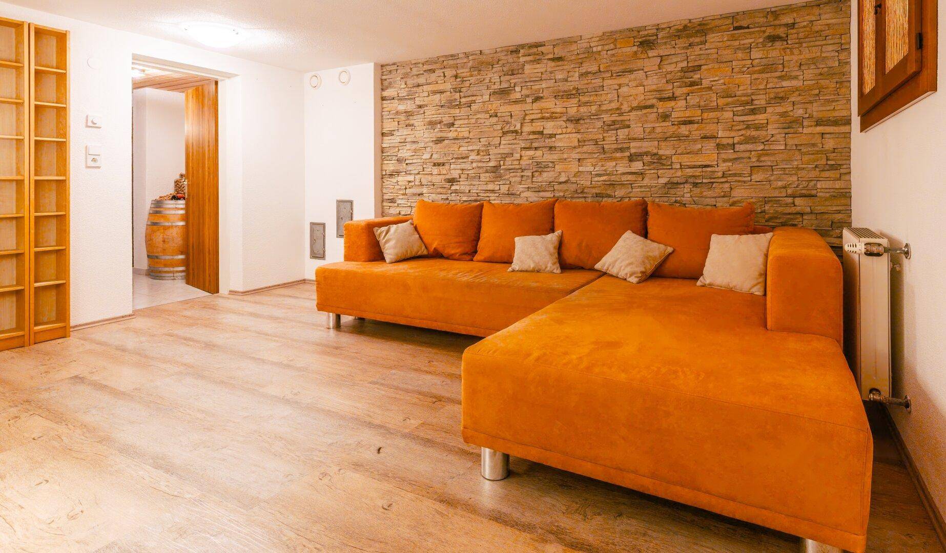 Wohnbereich im Untergeschoss mit Steinwand, großem Sofa und Holzboden.
