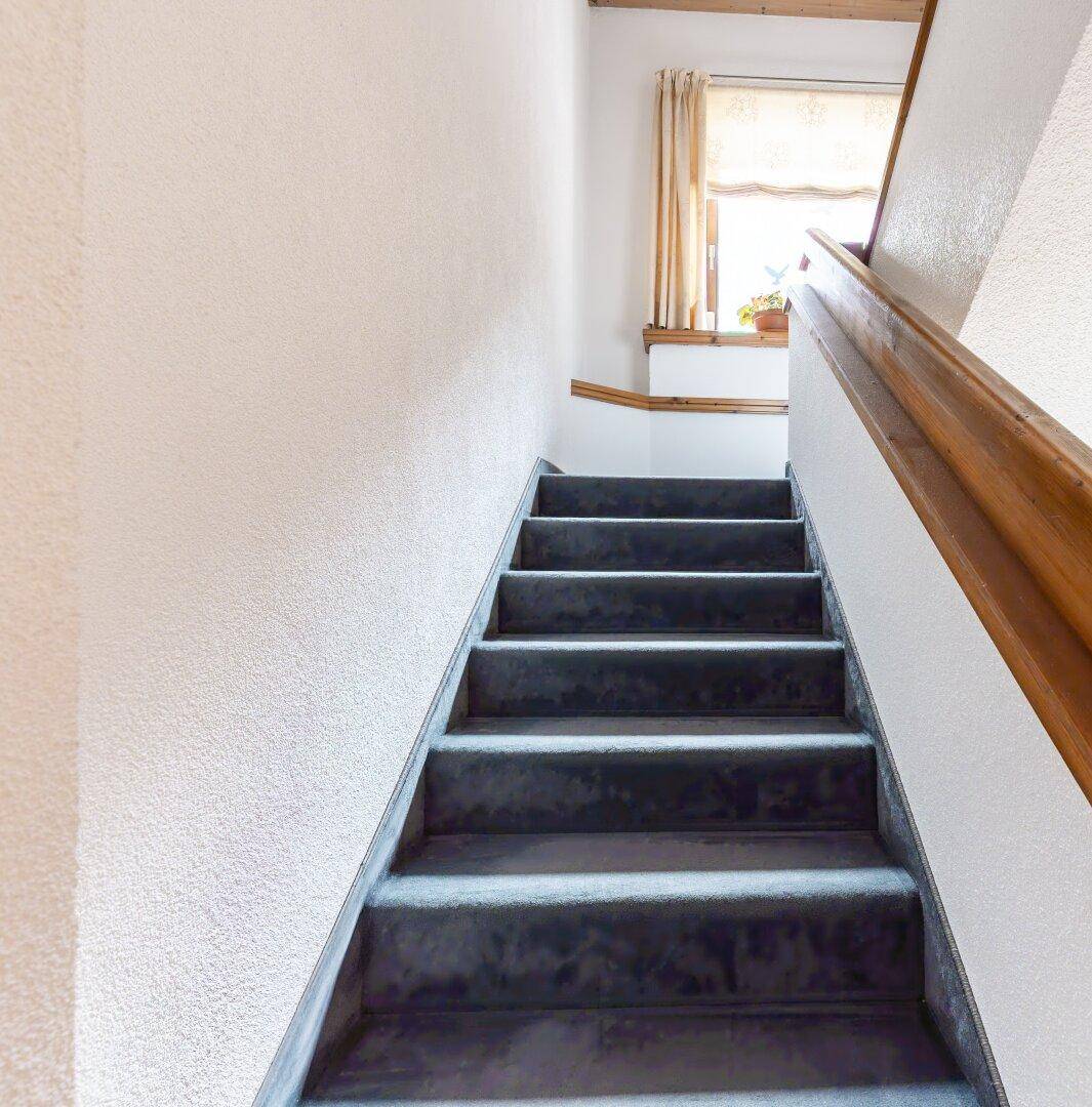 Treppenaufgang mit Teppichboden, Holzgeländer und Fenster für natürliches Licht.