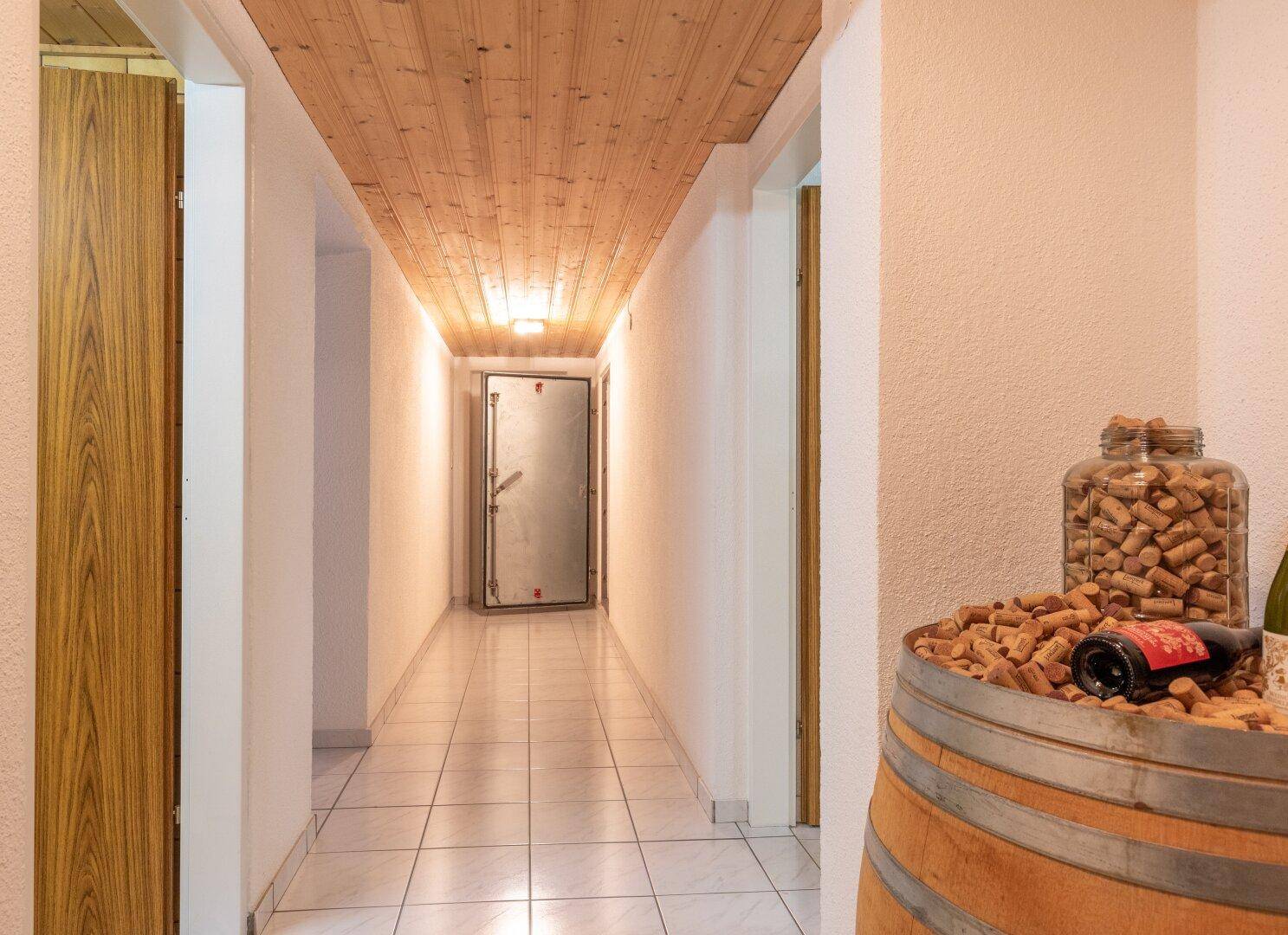 Langer Flur mit Holzbalkendecke, Fliesenboden und Weinfass-Dekoration.