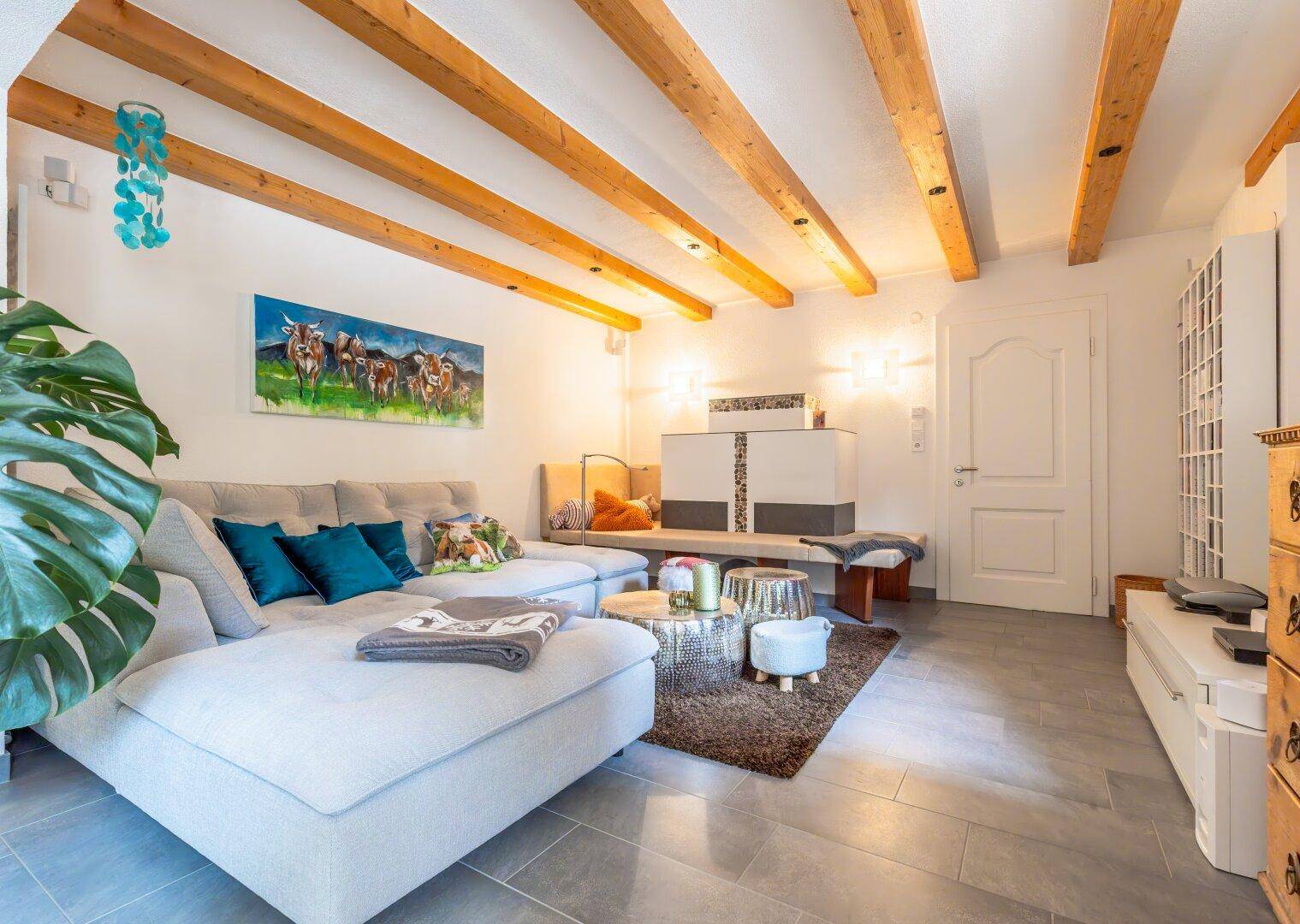 Gemütliches Wohnzimmer mit großem Sofa, Holzbalkendecke und Fliesenboden.
