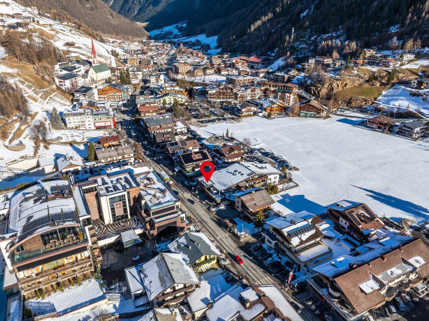 Weitläufige Luftaufnahme einer verschneiten Stadt in einem Tal, umgeben von majestätischen Bergen unter blauem Himmel.
