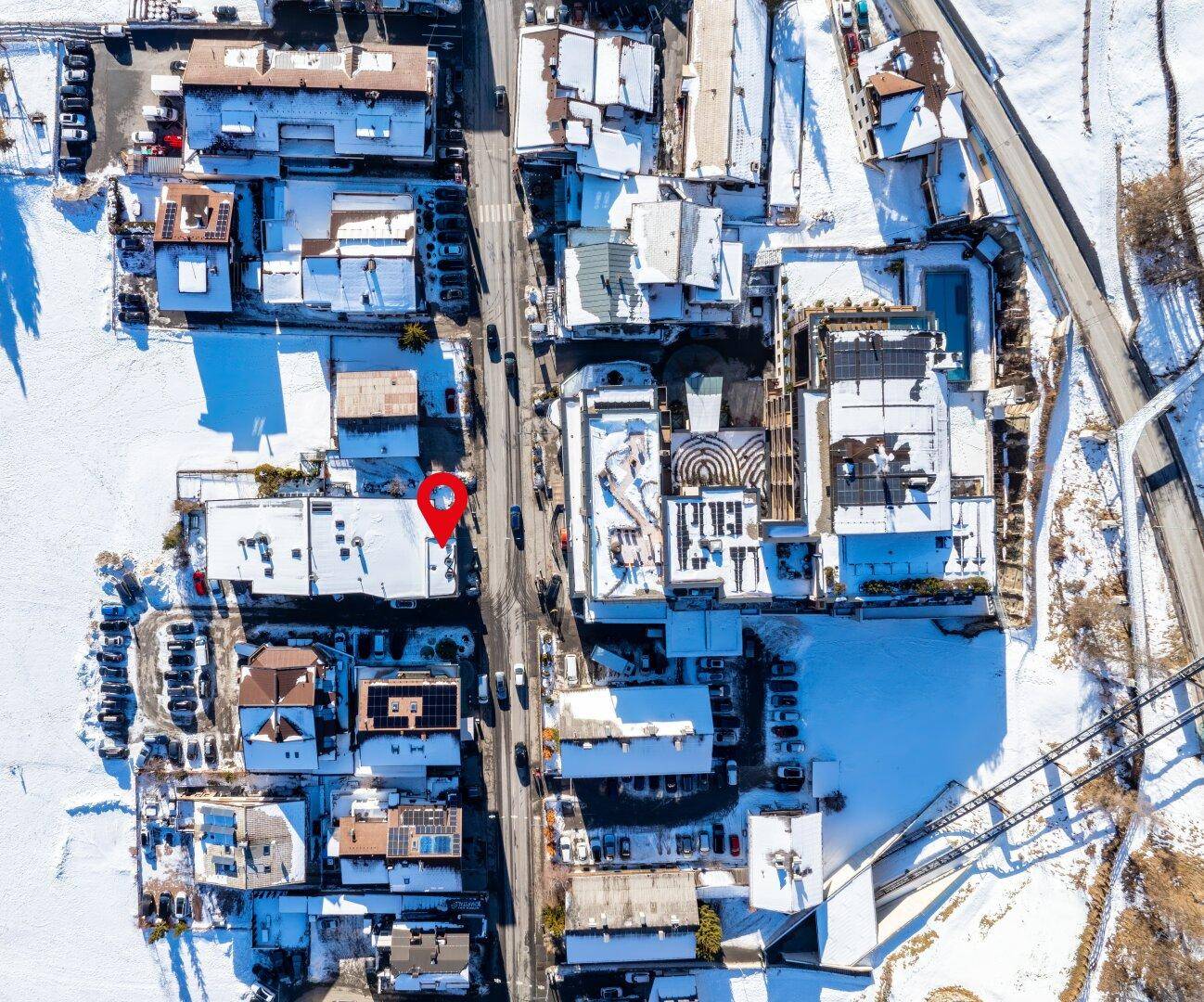 Senkrechte Luftaufnahme der verschneiten Dächer einer Stadt, mit Straßen und Parkplätzen, die sich durch die Winterlandschaft ziehen.